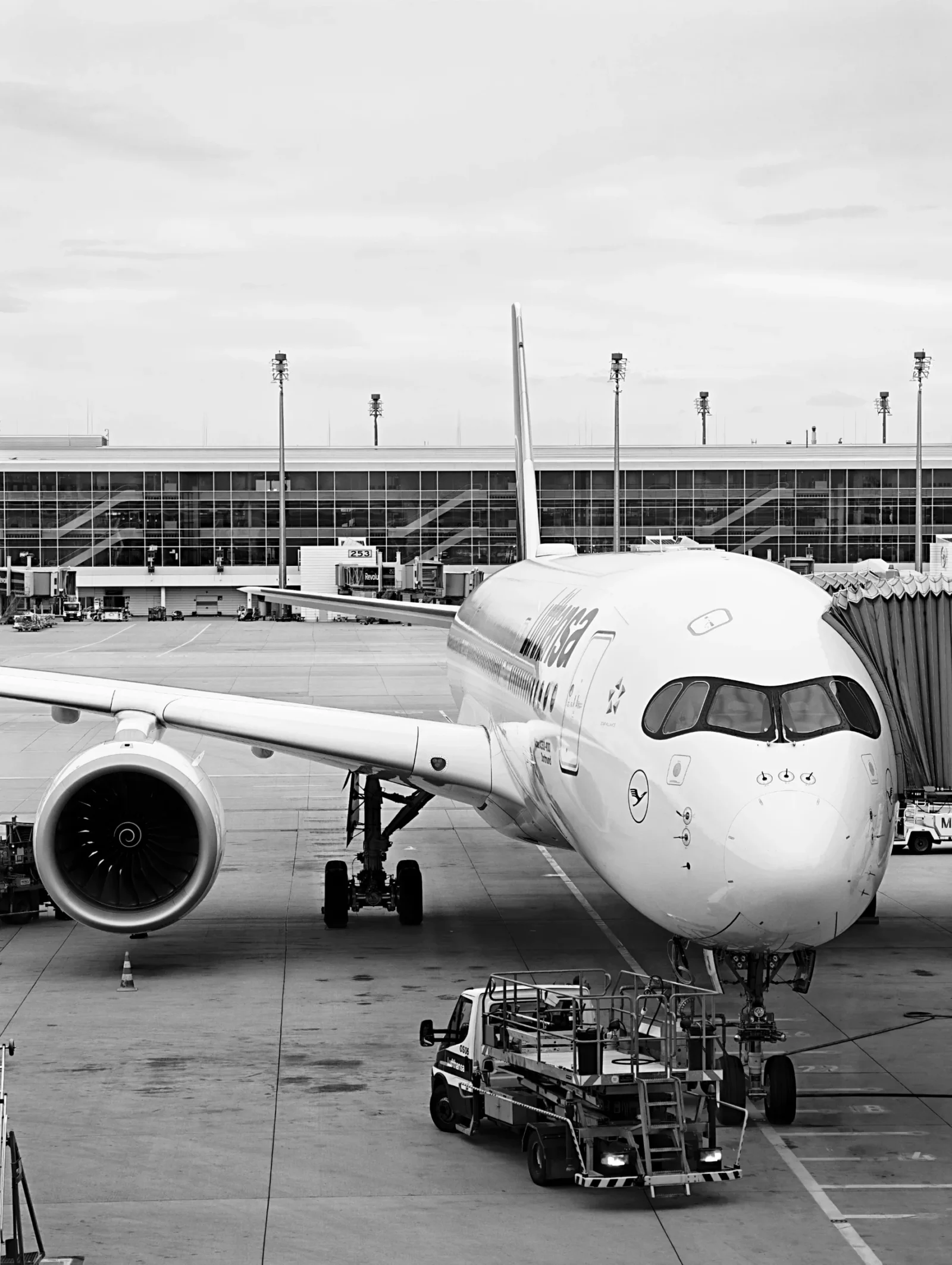 Black and white photograph of a Lufthansa Airbus A350 at a pier at Munich with the glass terminal behind.