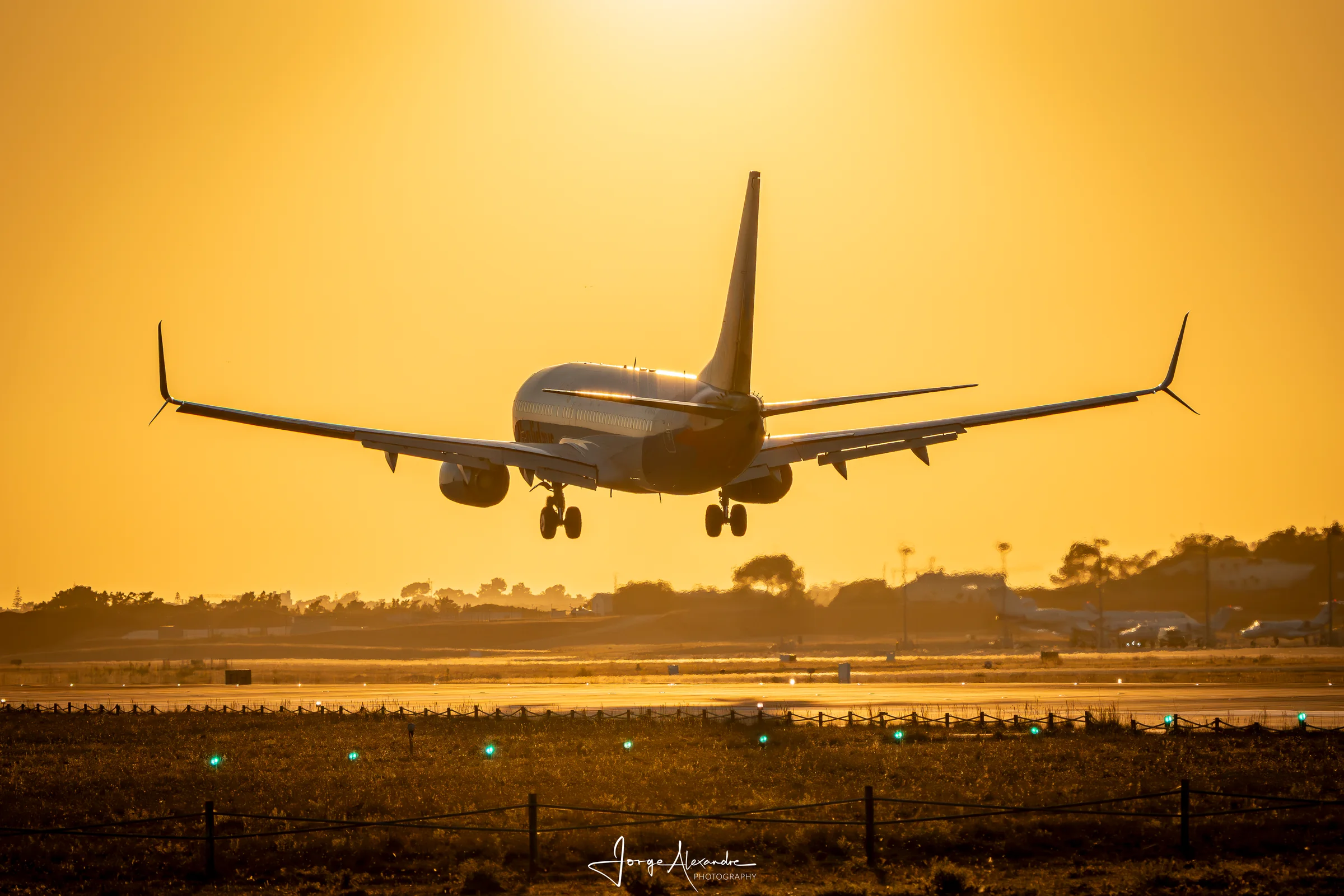 Boeing 737 on final approach silhouetted against an amber sunset sky, landing gear extended.
