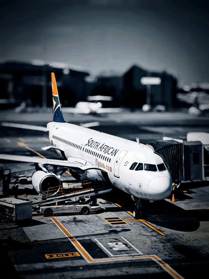 South African Airways Airbus at a jet bridge with a blurred dark terminal behind and orange taxi lines in front.