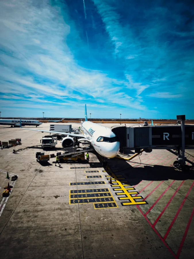 Airbus at a jet bridge at Faro Airport seen from above, ground crew working, under a vivid blue sky with cirrus.