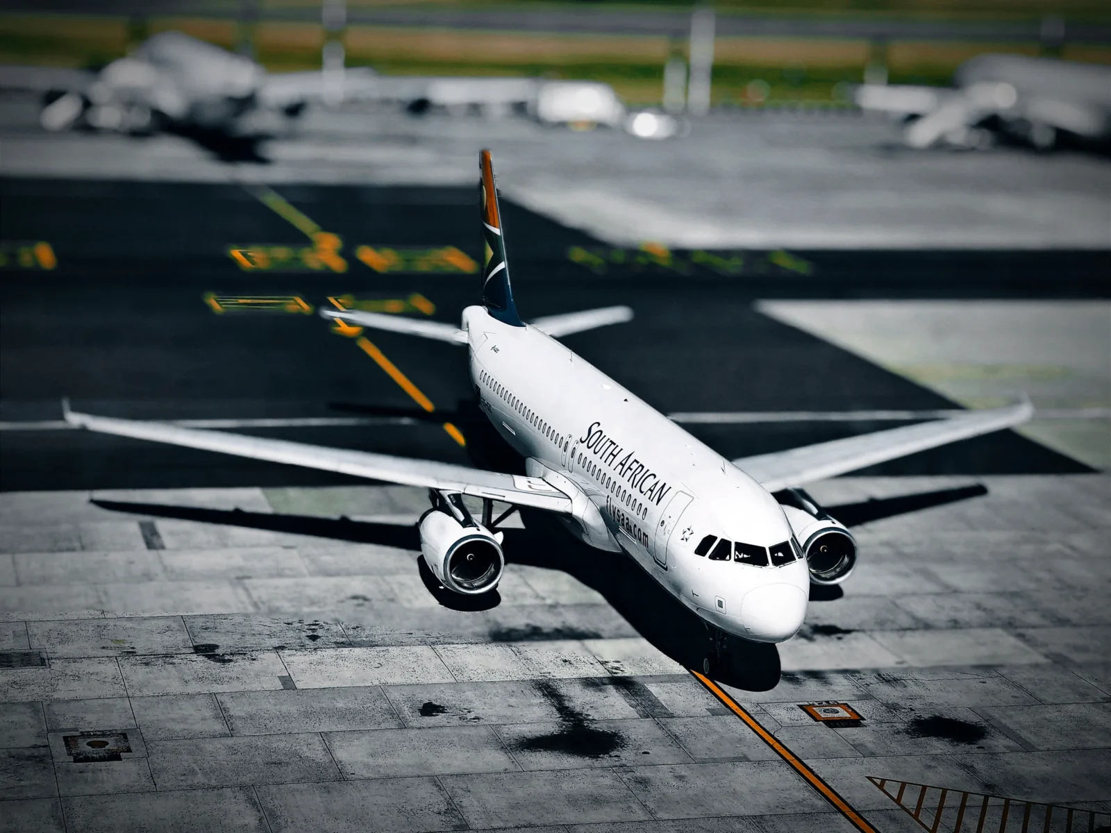 South African Airways Airbus turning on the apron at Cape Town International with a blurred, desaturated background.