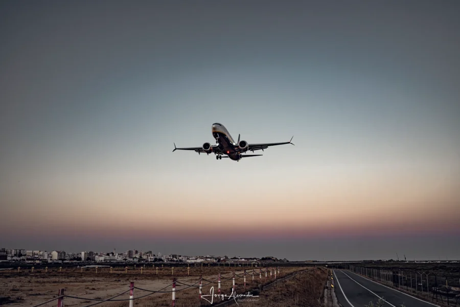 Boeing 737 climbing after take-off over a low city skyline at dusk, small against a smooth blue and pink sky.