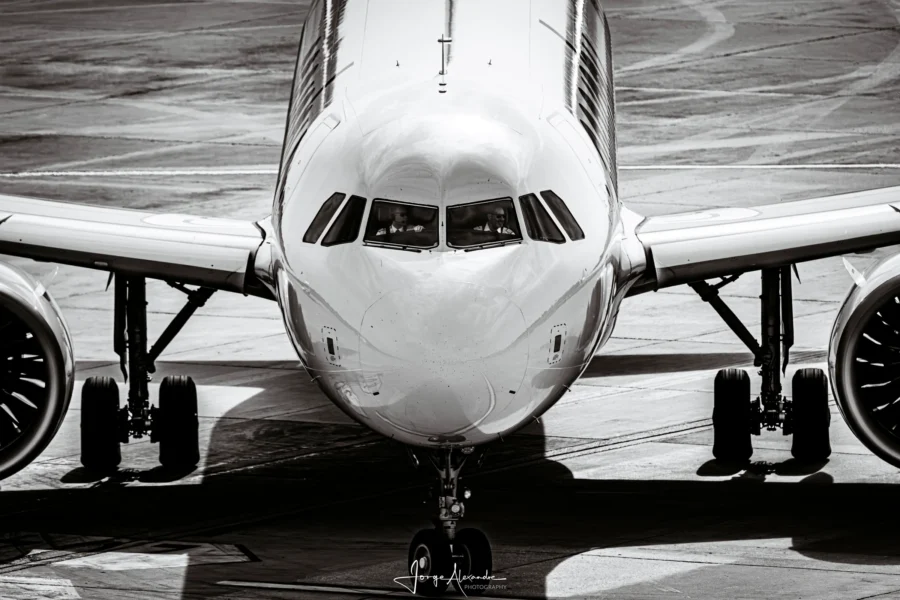 Airbus airliner taxiing directly towards the camera, nose and engines filling the frame, near-monochrome.