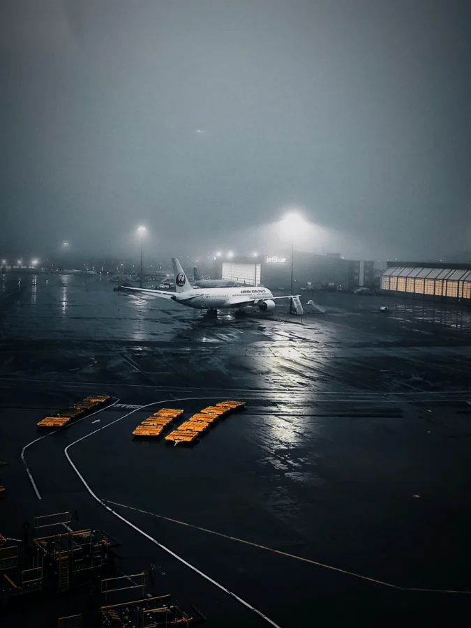 Japan Airlines widebody on a wet apron at Boston Logan in dense pre-dawn fog under glowing floodlights.