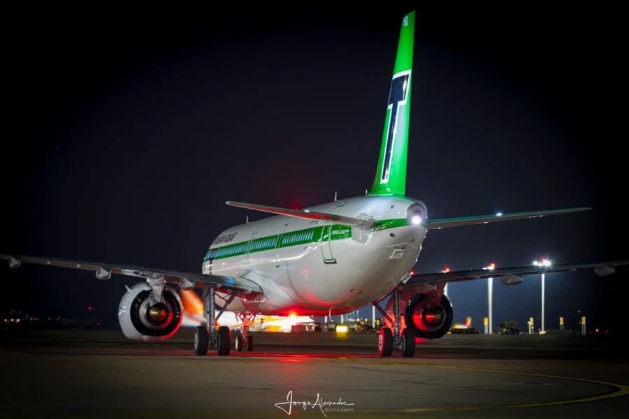 Transavia Holland retro-livery Airbus A321neo seen from behind at night, green tail lit, red beacon glowing.