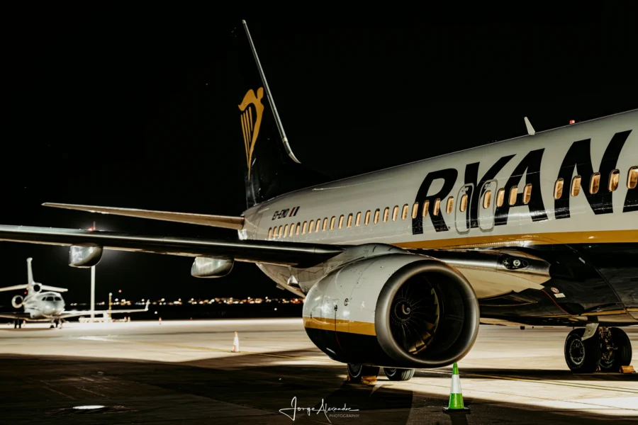 Ryanair Boeing 737 EI-EMD lit by floodlights at night, viewed low beneath the wing with the engine in the foreground.