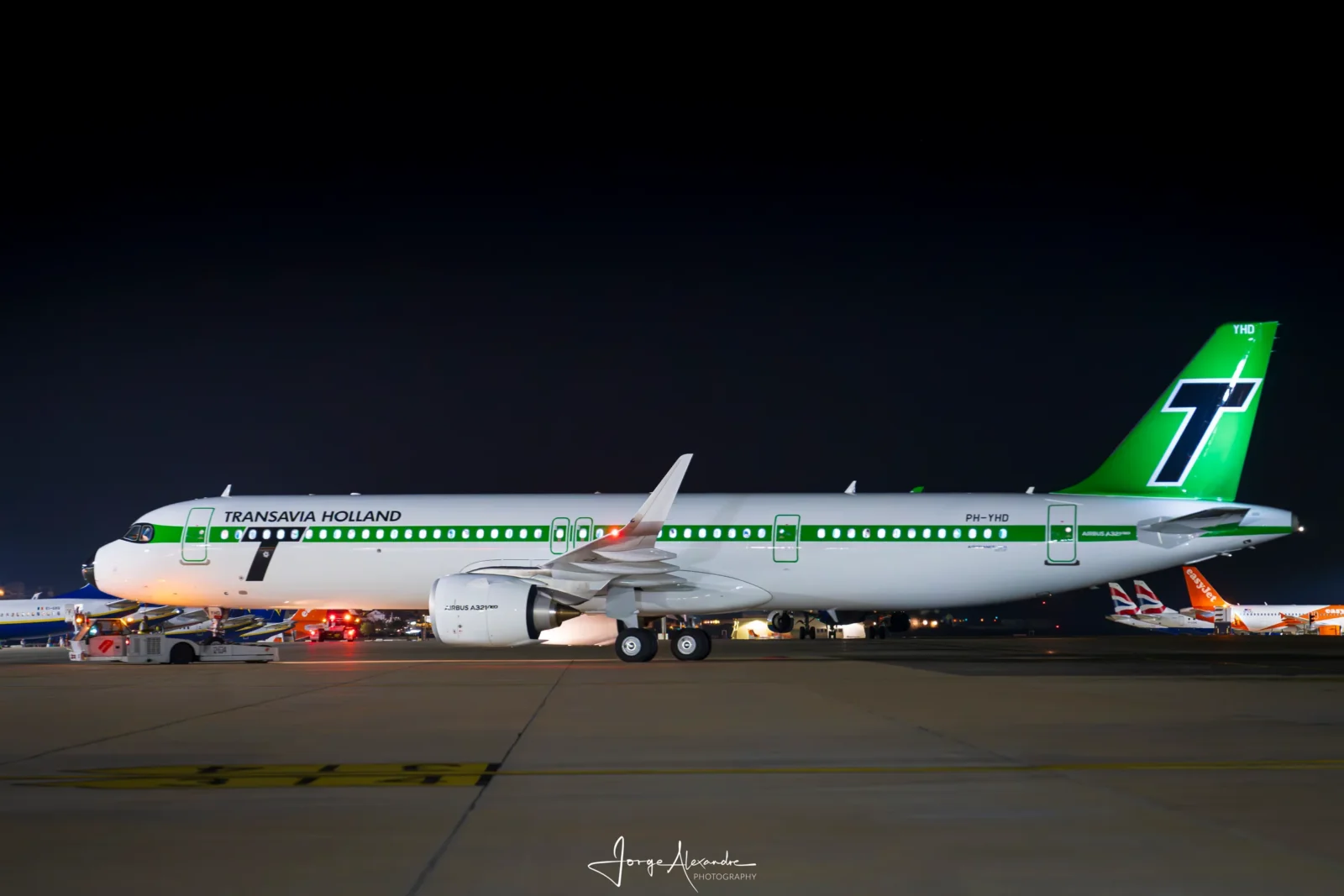 Side profile of Transavia retro-livery Airbus A321neo PH-YHD on the apron under a dark blue night sky.