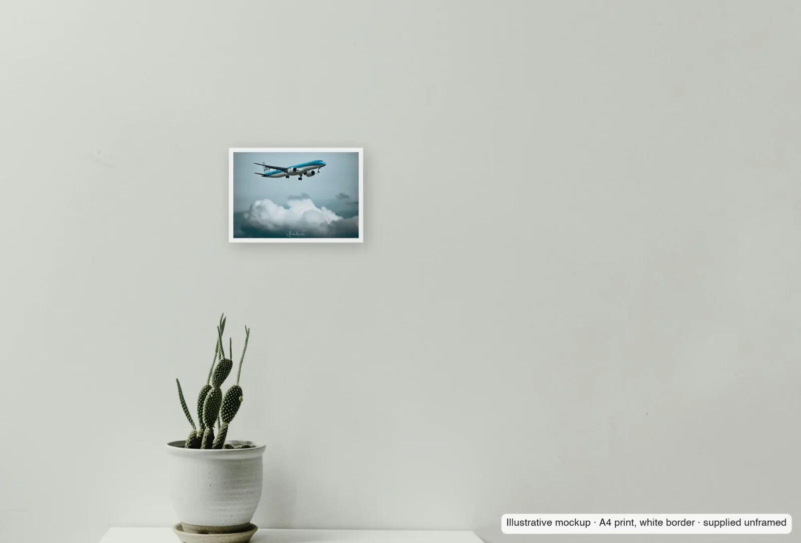Closer view of KLM over the cumulus as an unframed A4 white-border print above a sideboard.