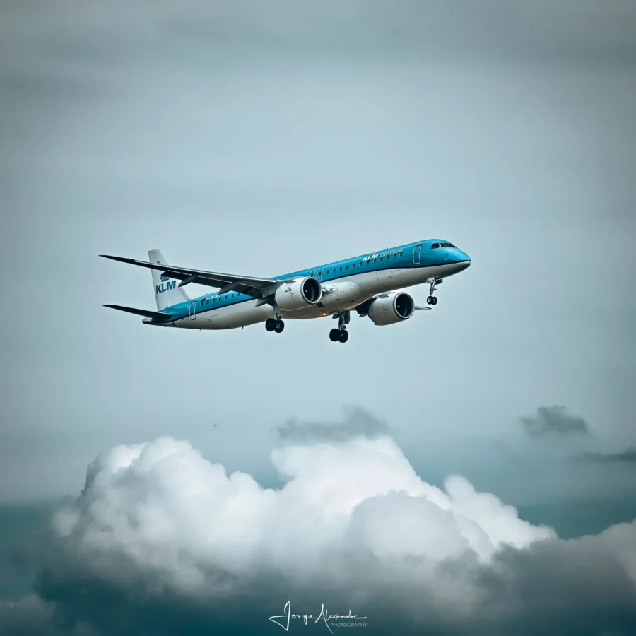 KLM Embraer regional jet on approach with gear down above a bank of white cumulus cloud.