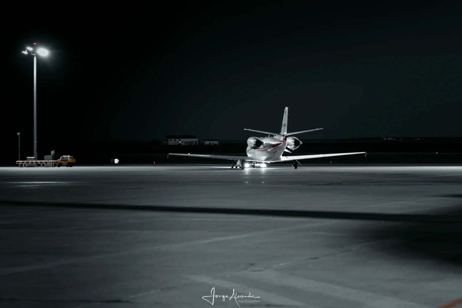 Small business jet taxiing alone across a dark apron at night beneath a single floodlight mast.