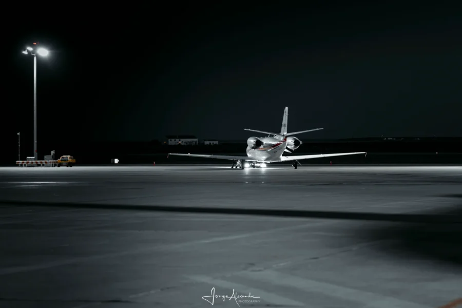 Small business jet taxiing alone across a dark apron at night beneath a single floodlight mast.