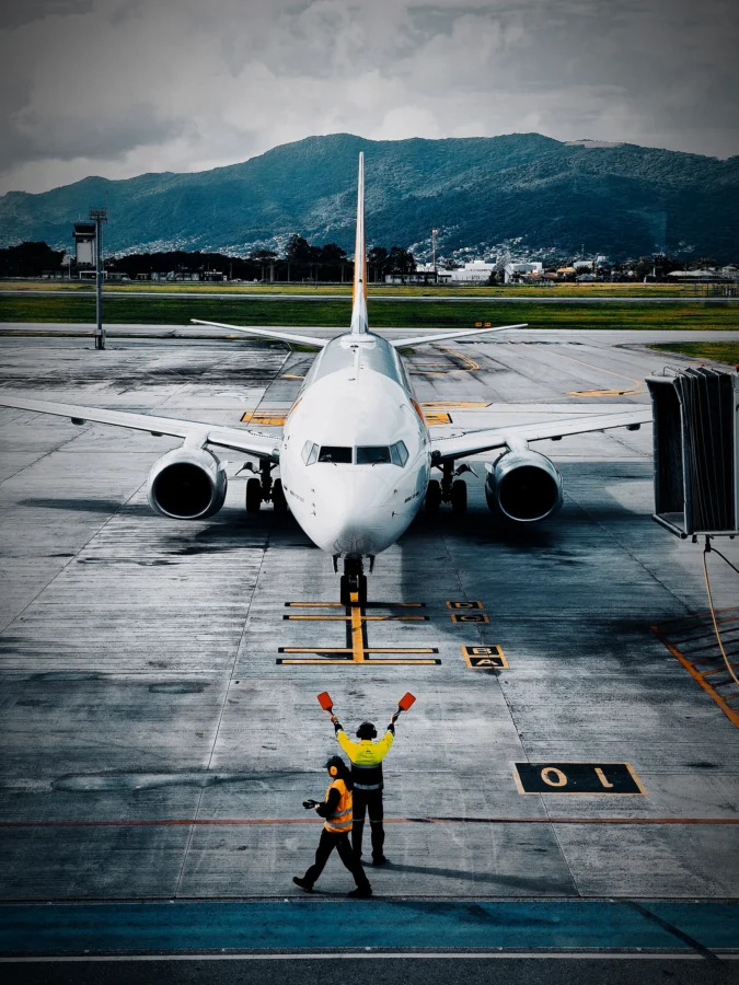 Marshallers with orange paddles guiding a Boeing 737 onto its stand at Florianópolis with mountains behind.