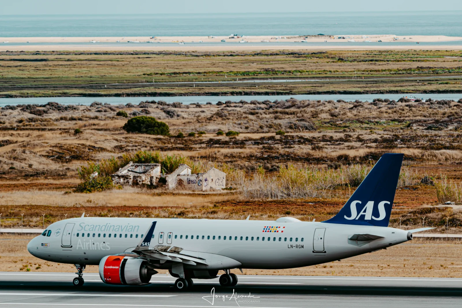 SAS Airbus A320neo LN-RGM on the runway with dunes, ruined cottages, marsh and the sea layered behind.