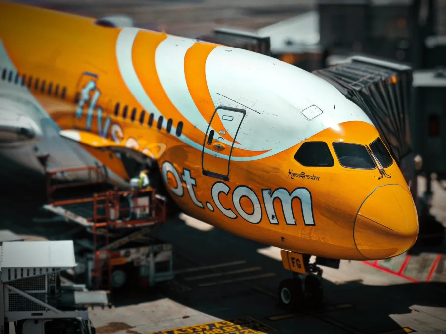 Orange nose of a Scoot Boeing 787 at a gate at Singapore Changi with large white lettering.