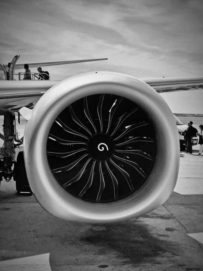 Black and white close-up of a jet engine fan at Faro Airport with passengers boarding on stairs above the wing.