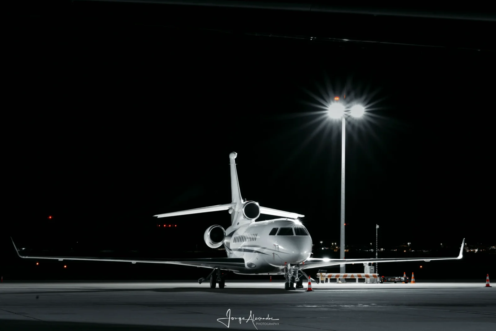 Dassault Falcon business jet parked alone at night under a floodlight mast with a starburst flare.