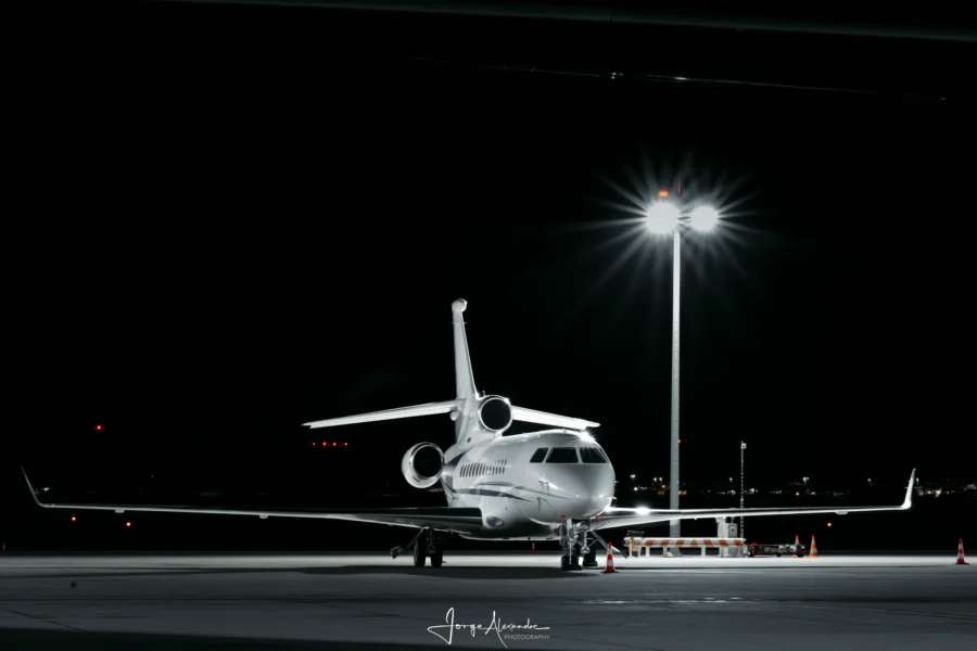 Dassault Falcon business jet parked alone at night under a floodlight mast with a starburst flare.