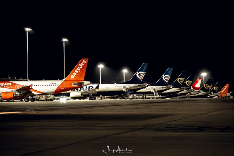 Row of parked airline tails at night, easyJet and Ryanair, under floodlight masts.