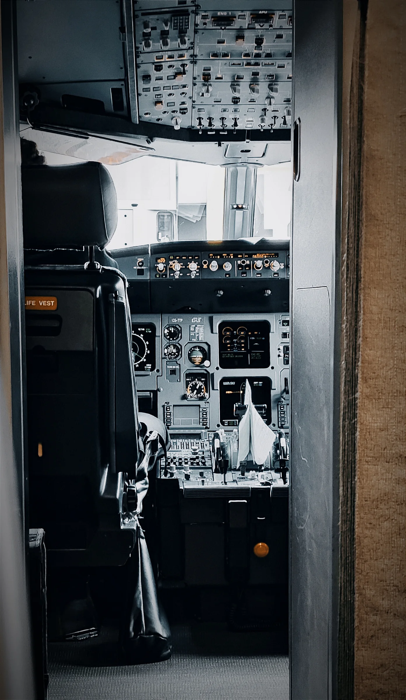 View through an open aircraft flight-deck door showing the captain's seat, overhead panel and instruments.