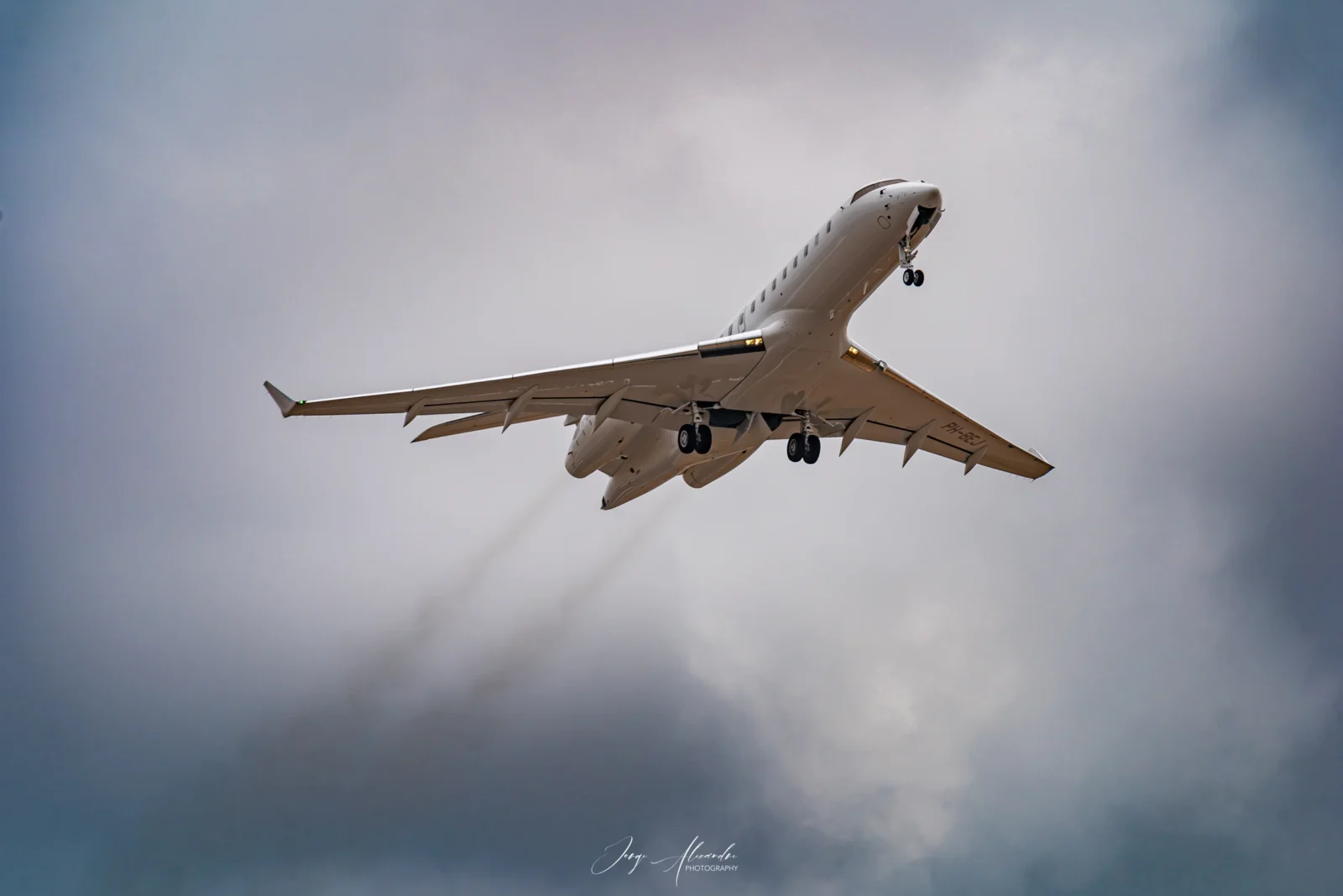 Business jet climbing steeply after take-off from Faro with exhaust trails against grey-blue clouds.
