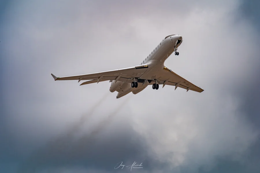 Business jet climbing steeply after take-off from Faro with exhaust trails against grey-blue clouds.