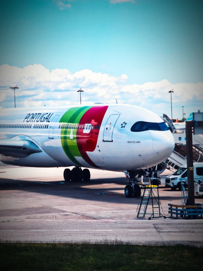TAP Air Portugal Airbus widebody named Vasco da Gama at a stand at Lisbon Airport under a blue sky.